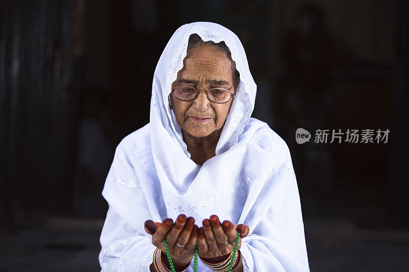 Senior Muslim Woman praying, with prayer beads beads in her hands